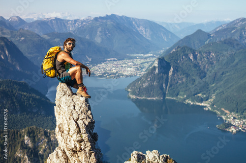 sporty male hiker sitting on top of a pinnacle with austrian seascape in the back