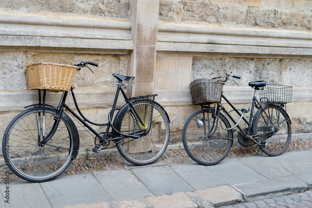 A pair of bicycles with baskets leaning on a wall A pair of bicycles with baskets leaning on a wall
