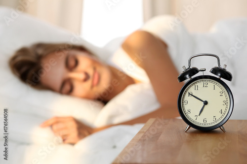 Wallpaper Mural Beautiful young woman sleeping and smiling while lying in bed comfortably and blissfully on the background of alarm clock is going to ring. Sunbeam dawn  on her face. Torontodigital.ca