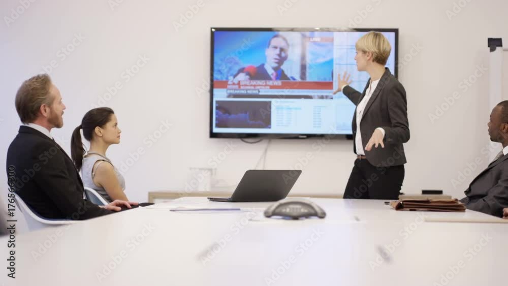 Business executives in boardroom meeting, TV with news report in background Business executives in boardroom meeting, TV with news report in background