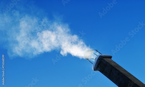 rauch aus einem schornstein aufsteigend/qualmender rauchfang vor tief blauem himmel/heizen im winter, globale erderwärmung photo