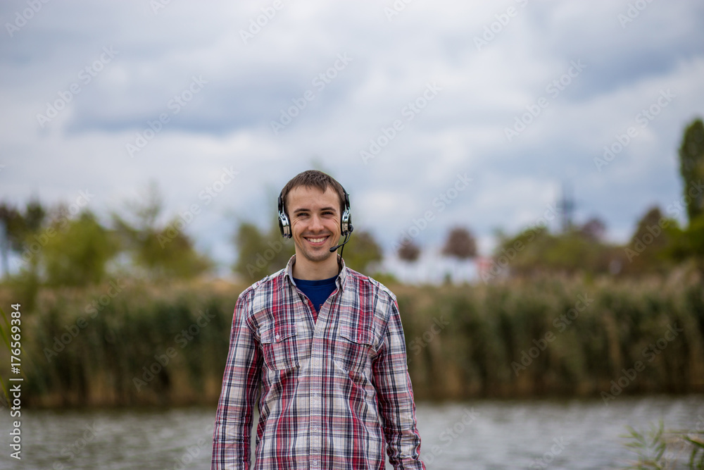 Portrait of a handsome smiling customer service operator wearing a headset standing on river pier