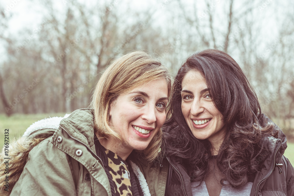 Two beautiful young women talking, smiling and having fun outdoors in a cold autumn day. Natural daylight, natural skin, natural background. Two beautiful young women talking, smiling and having fun outdoors in a cold autumn day. Natural daylight, natural skin, natural background.