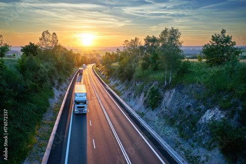 Three trucks driving on the highway in a rural landscape at sunset. View from above.