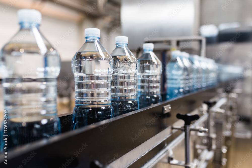 Bottling plant - Water bottling line for processing and bottling carbonated water into blue bottles. Selective focus. Bottling plant - Water bottling line for processing and bottling carbonated water into blue bottles. Selective focus.