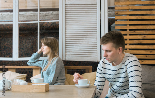 Young nice couple sitting in cafe wrapped in cozy blanket drinking tea. Love story of a girl and a boy. Man and woman embrace one another on a terrace. Sweet couple choosing what to read on a tablet.