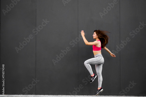 Sport fitness girl in fashion sportswear jumping in the street, on gray wall background ,outdoor sports. Urban style.