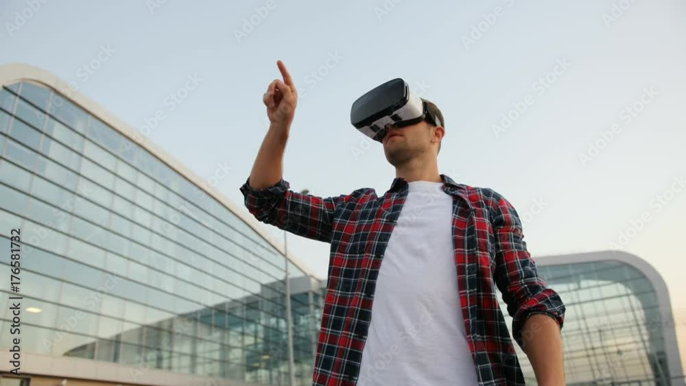 Portrait of a confident young man using a VR headset. Tapping the virtual screen. Blurred background.