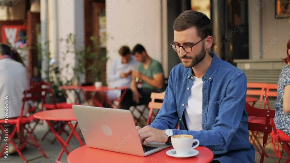 A portrait of a handsome young man working on a modern laptop in the cafe outdoors