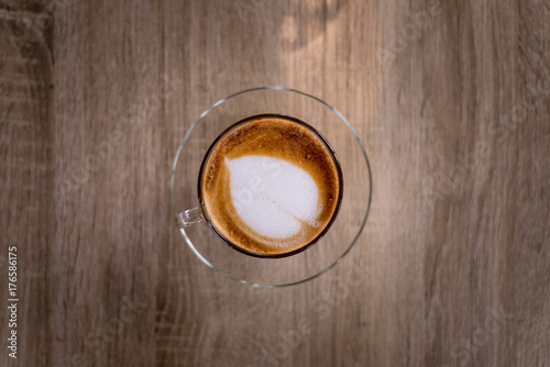 Hot coffee with heart make up on face of milk cream in glass cup on wooden table background, top view