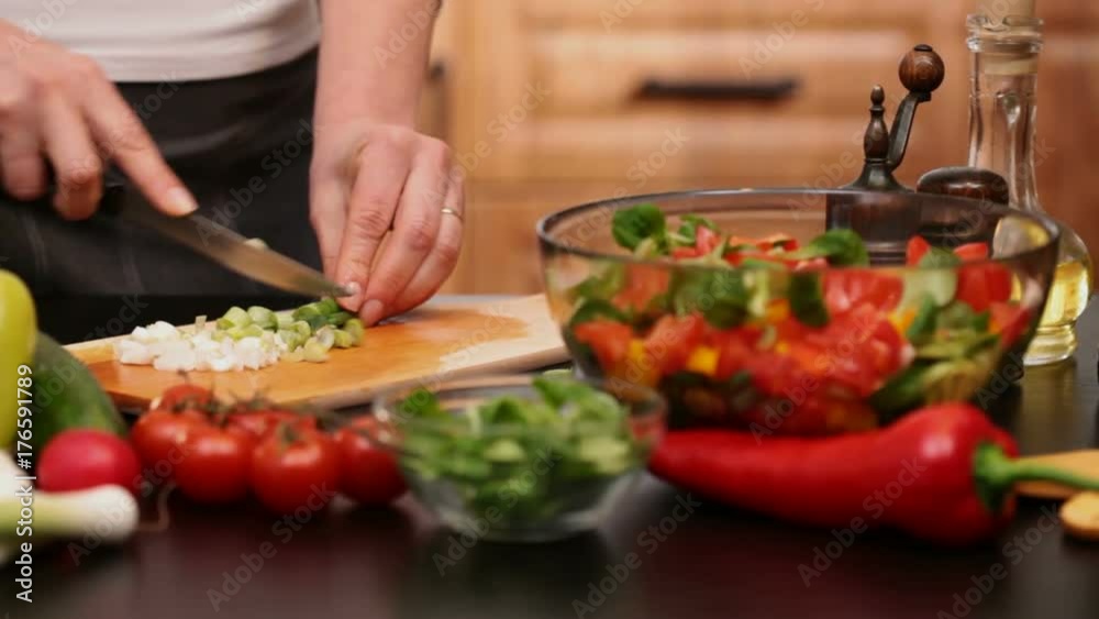 Woman hands chopping spring onions for a vegetables salad - side view of the cutting board at the kitchen table, camera zooming in Woman hands chopping spring onions for a vegetables salad - side view of the cutting board at the kitchen table, camera zooming in