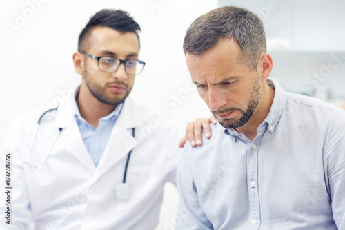 Unhappy patient looking downwards while doctor reassuring him