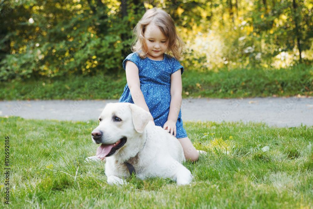 Little girl sitting on the grass with labrador retriever in the summer park Little girl sitting on the grass with labrador retriever in the summer park