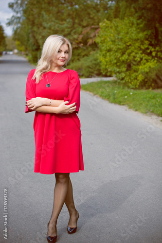 Portrait of pretty middle-aged woman in a red oversize dress in a cottage town, a beautiful blonde hair lady is walking in the open air