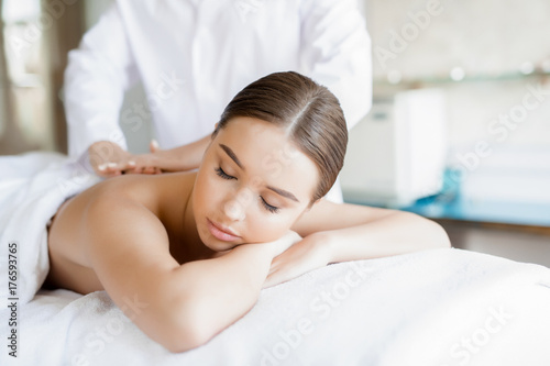 Relaxed young woman lying in spa salon and enjoying professional body massage