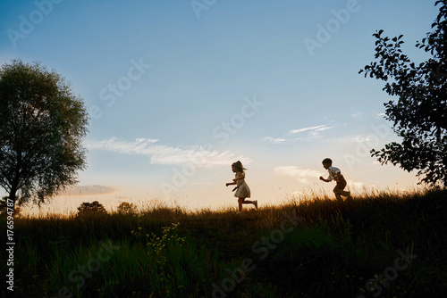 brother and sister running in the meadows at sunset