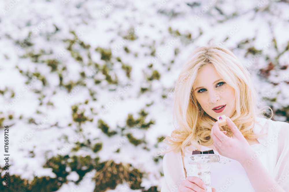 Blonde Frau isst Pralinen in Winterlandschaft Blonde Frau isst Pralinen in Winterlandschaft