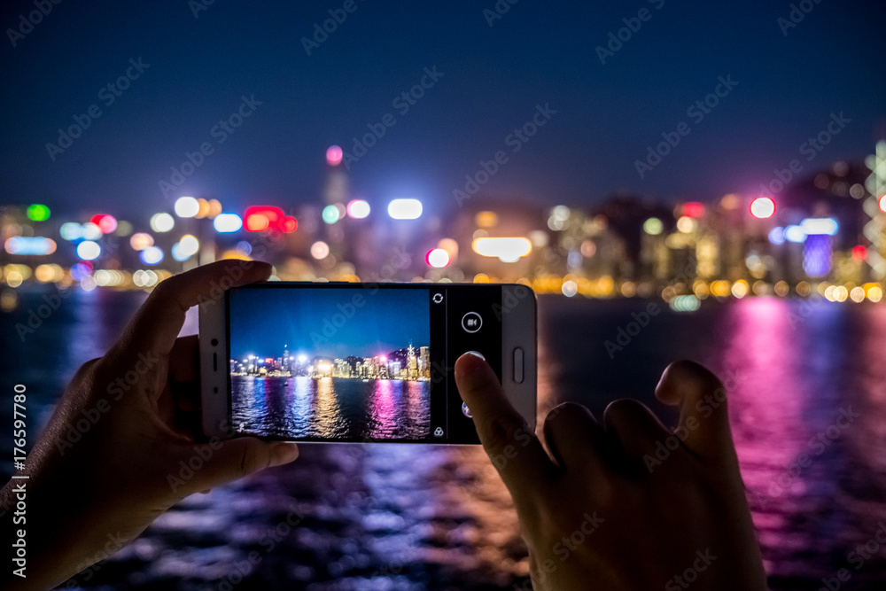 Fototapeta premium Woman using her Mobile Phone to take photo of city view, night light Background