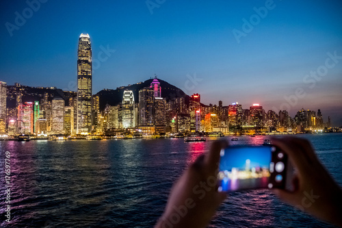 Woman using her Mobile Phone to take photo of city view, twilight Background