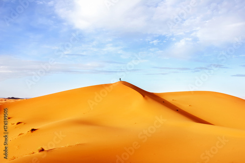 High sand dunes of the Sahara desert against a blue sky with clouds.