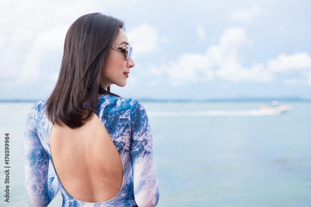 Young beautiful smart woman in swimsuit sportswear wear fashion sunglasses  with smile at the sea under blue sky. Summer lifestyle concept.