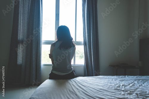 woman sitting on bed in room with light from window (abuse concept) photo