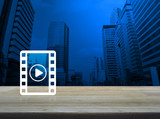 Play button with movie icon on wooden table over modern office city tower background, Cinema online concept