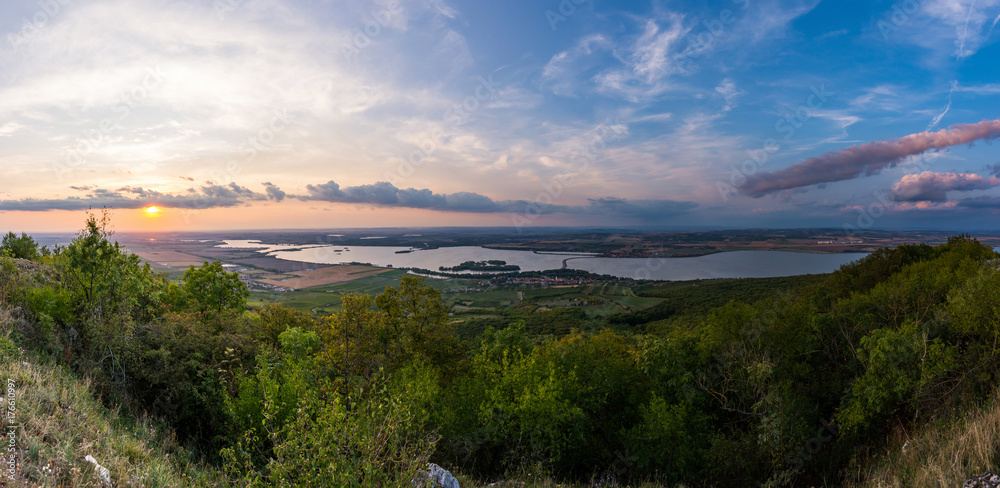 Lake landscape panorama in golden hour, sunset and beautiful clouds, plants and grass in foreground