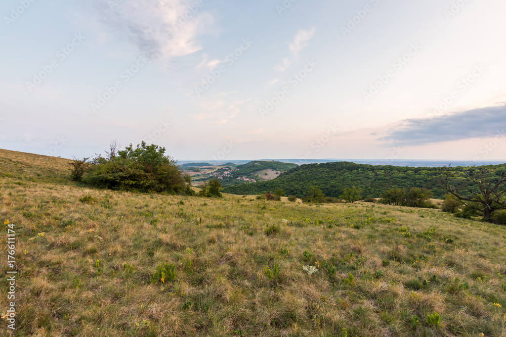 Sunset landscape panorama, hills in golden hour, small village in valley, beautiful colors and clouds.