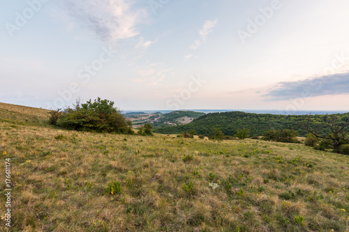 Sunset landscape panorama, hills in golden hour, small village in valley, beautiful colors and clouds.