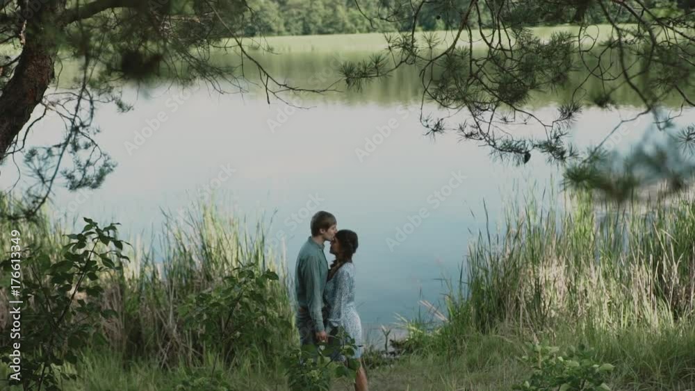 A loving couple is standing by the lake and looking at each other.Smiling couple.A young attractive couple walking through the forest with their happy dog.Slow motion. A loving couple is standing by the lake and looking at each other.Smiling couple.A young attractive couple walking through the forest with their happy dog.Slow motion.