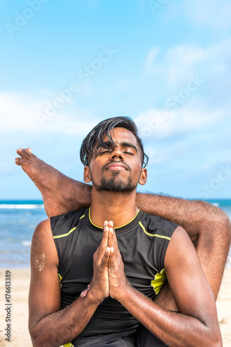 Asian yoga man practice yoga on the beach with a clear blue sky background. Yogi on the tropical beach of Bali island, Indonesia. © belart84