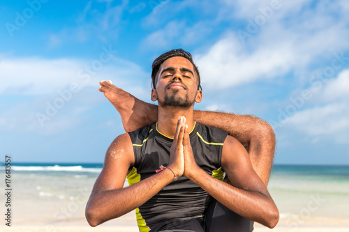 Asian yoga man practice yoga on the beach with a clear blue sky background. Yogi on the tropical beach of Bali island, Indonesia.