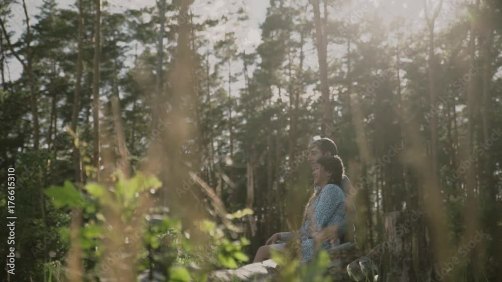 A young attractive couple walking through the forest with their happy dog.Couple in love play with the dog shiba in pine forest .Sunny weather.A loving couple is standing in sunset forest and looking A young attractive couple walking through the forest with their happy dog.Couple in love play with the dog shiba in pine forest .Sunny weather.A loving couple is standing in sunset forest and looking