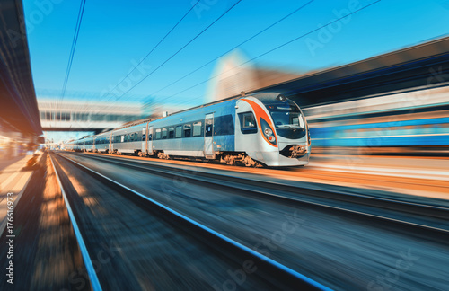 High speed train in motion at the railway station at sunset in Europe. Modern intercity train on the railway platform with motion blur effect. Industrial scene with moving passenger train on railroad