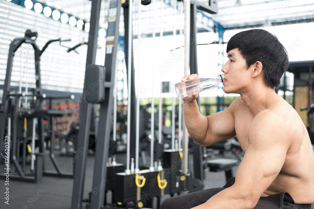 young man drinking water in fitness center. male athlete feeling thirsty after training in gym. sporty guy taking a break from working out in health club.
