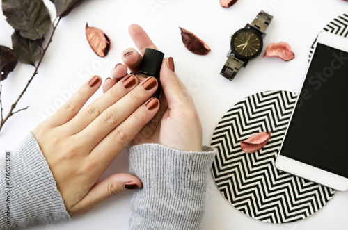 Obraz na plátně Female hands with nail polish on white background with mobile phone, watch and autumn petals