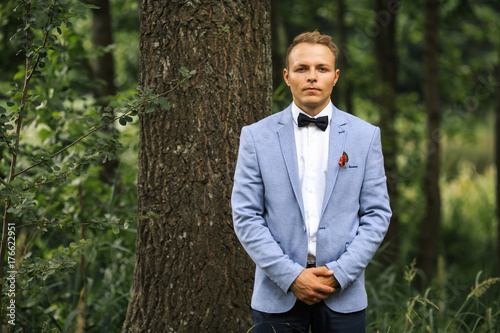 Young handsome groom in blue jacket is posing on a wedding walk in the forest. Wedding day.