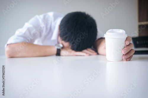 Tired businessman sleeping at work in modern office with hand holding coffee cup, people dozing on workplace