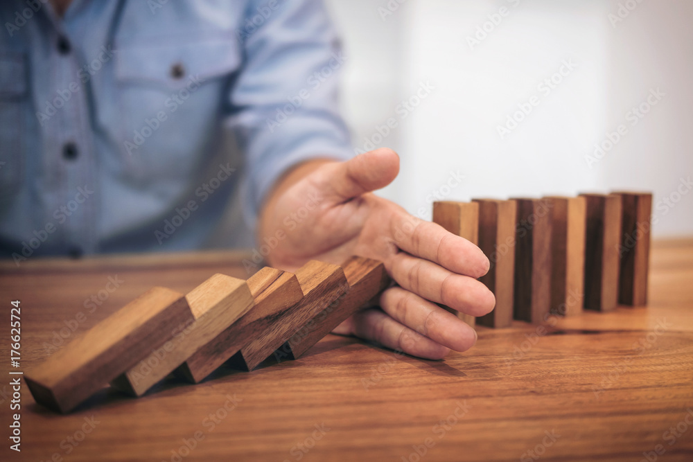 Risk and strategy in business, Close up of businessman hand stopping wooden block from falling in the line of domino Risk and strategy in business, Close up of businessman hand stopping wooden block from falling in the line of domino