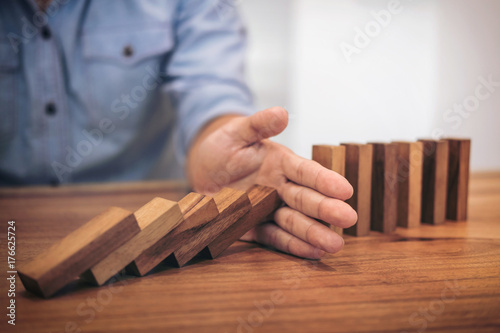 Risk and strategy in business, Close up of businessman hand stopping wooden block from falling in the line of domino