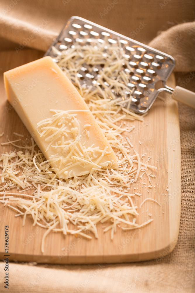 Parmesan Cheese and Grater Medium. an wider view of a block wedge of  parmesan cheese with shredded pieces all around and a metal cheese grater  on a cutting board Stock Photo