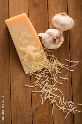 Shredded Parmesan and Wedge with Garlic Above. an above shot looking down on a wedge of parmesan cheese and two cloves of garlic with shredded slices of cheese on top