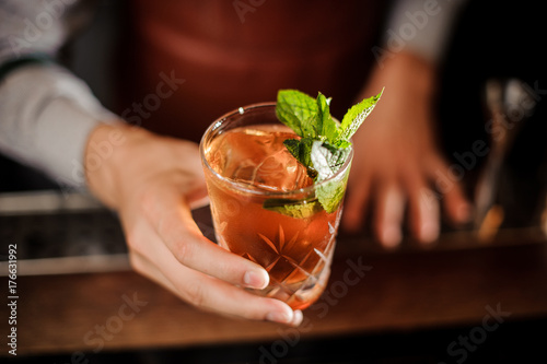 Bartender is holding a shot glass with alcoholic drink and mint