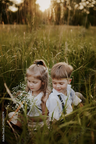 Twins brother and sister sitting in a meadow against the sunset background