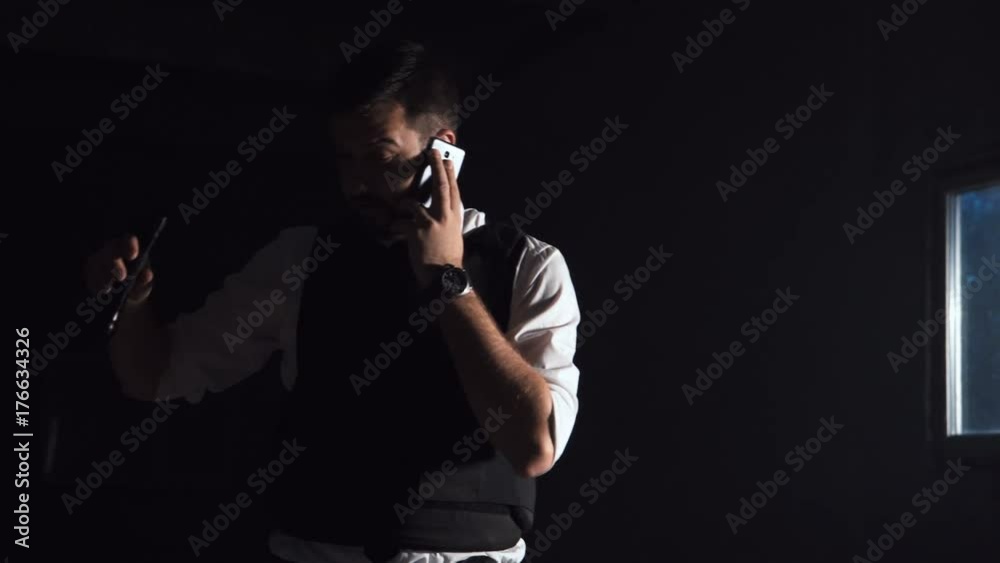 Vigilant and courageous police investigator talking on mobile phone while searching for a dangerous suspect indoor in the night Vigilant and courageous police investigator talking on mobile phone while searching for a dangerous suspect indoor in the night