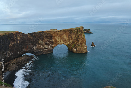 Amazing black arch of lava standing in the sea on small peninsula. Popular tourist attraction. Unusual and gorgeous scene. Location Sudurland, cape Dyrholaey, coast of Iceland, Europe. Beauty world.