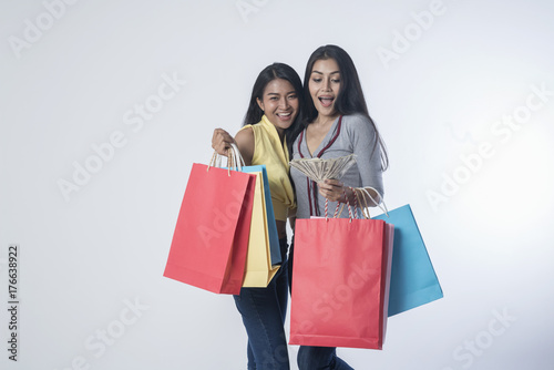 shopping, sale and gifts concept - two smiling teenage girls with shopping bags and cash money