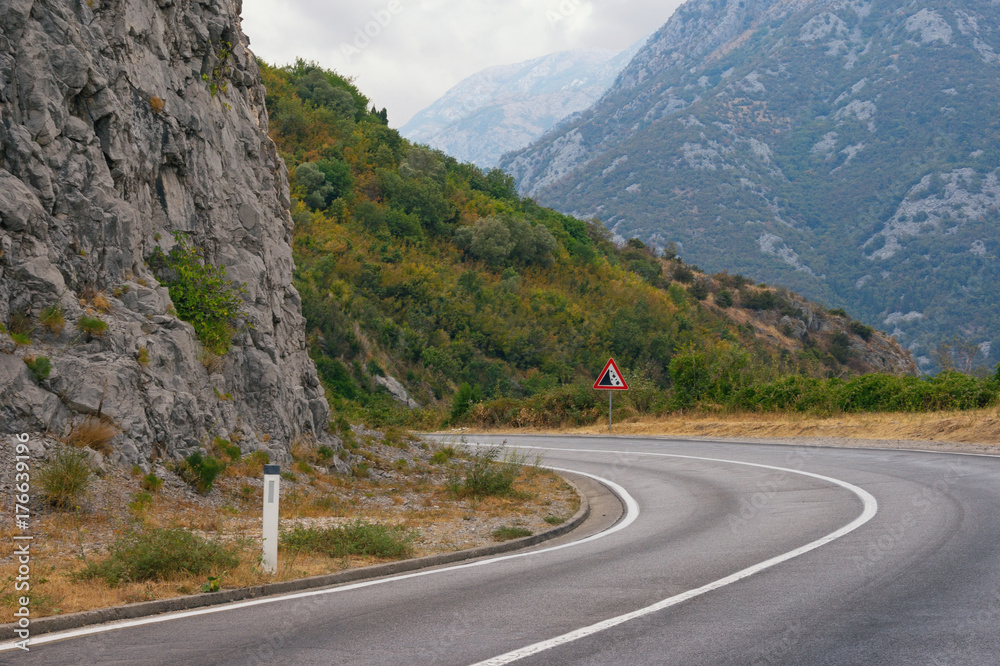 Fototapeta premium Sharp turn of the road with a sign of falling stones. Balkans, Montenegro