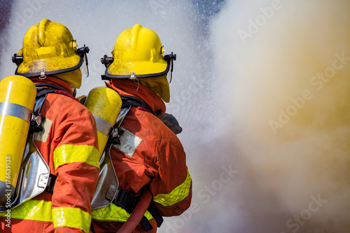 two firefighters water spray by high pressure nozzle surround with dark smoke and copy apace